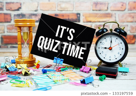 It's Quiz Time text on paper card with alarm clock and stationary on wooden background 133197559