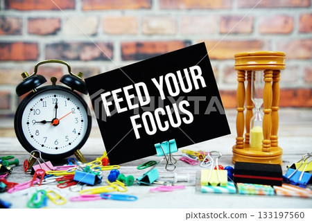 Feed Your Focus text on paper card with alarm clock and stationary on wooden background Feed Your Focus text on paper card with alarm clock and stationary on wooden background 133197560
