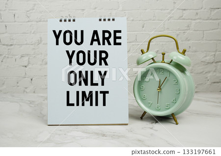 "You Are Your Only Limit" with green vintage alarm clock against a white brick wall background. 133197661