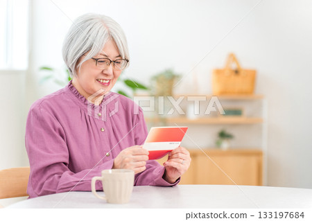 Smiling senior woman looking at her savings passbook in the living room of her home (retirement funds, asset management, deposits, income, living expenses) Smiling senior woman looking at her savings passbook in the living room of her home (retirement funds, asset management, deposits, income, living expenses) 133197684