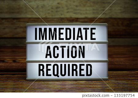 Lightbox with text "Immediate Action Required" on wooden background 133197754