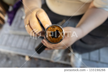 A person's hands hold a section of an old, rusted water pipe, revealing heavy rust and mineral deposits. The buildup of limescale and rust obstructs the flow of water through the pipe. A person's hands hold a section of an old, rusted water pipe, revealing heavy rust and mineral deposits. The buildup of limescale and rust obstructs the flow of water through the pipe. 133198266
