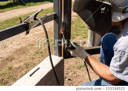 Male adult welding metal frame outdoors with protective gear. National Welding Month 133198525
