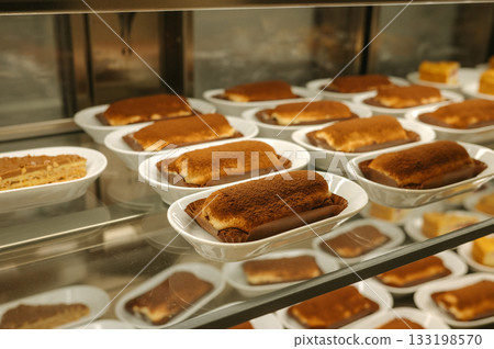 Row of delicious tiramisu desserts in white plates on display shelf Row of delicious tiramisu desserts in white plates on display shelf 133198570