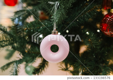 Pink doughnut ornament hanging on green christmas tree with lights and red bauble Pink doughnut ornament hanging on green christmas tree with lights and red bauble 133198576