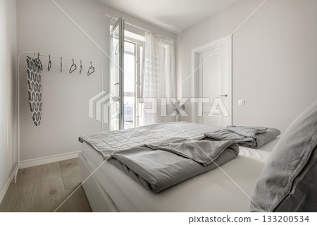 Bright minimalist bedroom with open window and gray bedding 133200534