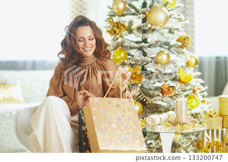 Woman Opening Star-Patterned Gift Bag by Christmas Tree Woman Opening Star-Patterned Gift Bag by Christmas Tree 133200747