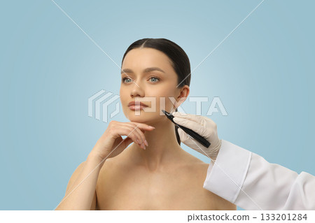 A beautician prepares a client for a facial procedure with markings 133201284
