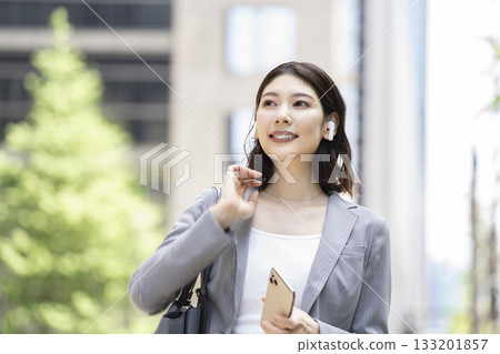 Businesswoman wearing earphones and holding a smartphone Businesswoman wearing earphones and holding a smartphone 133201857