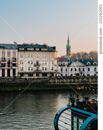 Beautiful view of church and Vistula River with colorful buildings at sunset in Krakow, Poland, creates picturesque urban landscape. Historic skyline with golden sunset and vibrant architectural charm Beautiful view of church and Vistula River with colorful buildings at sunset in Krakow, Poland, creates picturesque urban landscape. Historic skyline with golden sunset and vibrant architectural charm 133202001