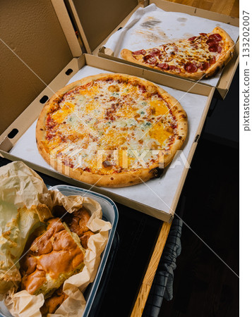 Two whole pizzas featuring variety of toppings alongside some focaccia bread sit in plastic container on kitchen counter, awaiting enjoyment for lunch or dinner. Two big pizzas and focaccia bread Two whole pizzas featuring variety of toppings alongside some focaccia bread sit in plastic container on kitchen counter, awaiting enjoyment for lunch or dinner. Two big pizzas and focaccia bread 133202007