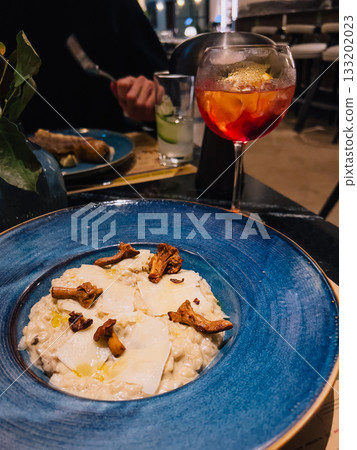 Creamy mushroom risotto with parmesan and chanterelle mushrooms, elegantly plated in restaurant, accompanied by cocktail and customer enjoying their meal. Dining restaurant setting. Dating concept 133202023