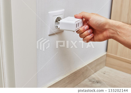 male hand insert a plug of the phone charger into socket at home 133202144