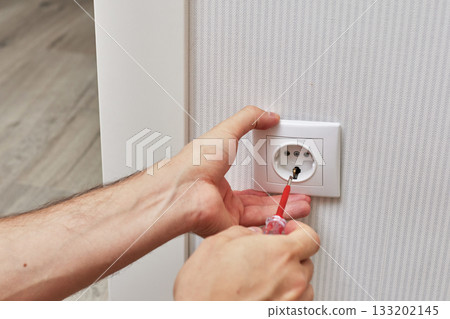 male hands installing electrical wall outlets with a screwdriver at home 133202145