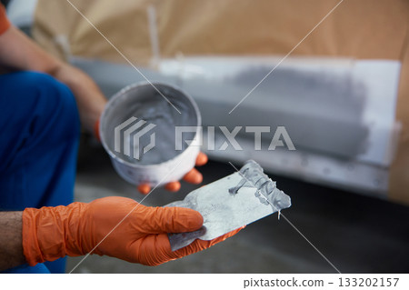 Closeup of technician is meticulously prepping a car panel with primer in a garage workshop 133202157