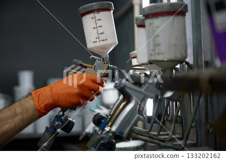 An industrial paint spray gun being used by a technician wearing protective gloves inside a workshop 133202162