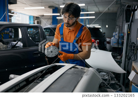Auto body technician sanding car panel in workshop - repair and refinishing process 133202165