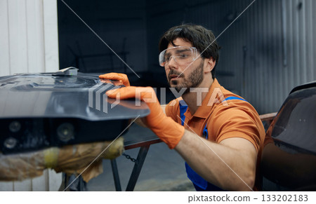 Technician worker skillfully restoring a car door in a busy garage workshop space 133202183