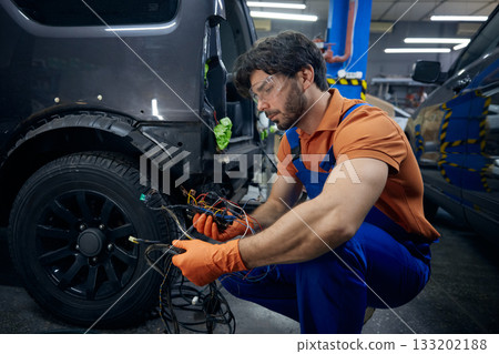 Mechanic repairing car wiring in auto workshop 133202188