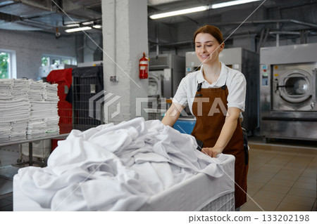 A woman worker pushes a cart full of white sheets in a laundromat A woman worker pushes a cart full of white sheets in a laundromat 133202198