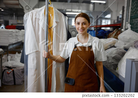 A woman worker in an apron holds a hanger with clothes, showing her role 133202202