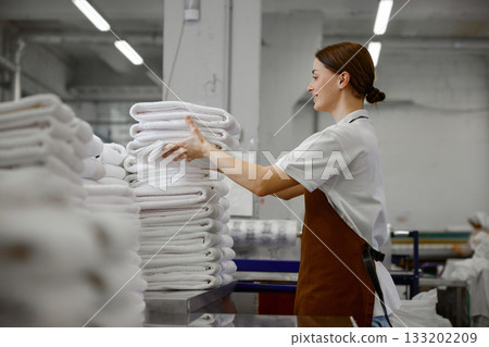 A woman worker is stacking towels neatly on a table in a laundromat 133202209