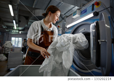 A woman is in the process of putting various clothes into a washing machine 133202214