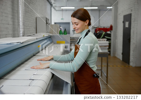 A young woman worker is ironing towels on a table in a laundromat A young woman worker is ironing towels on a table in a laundromat 133202217