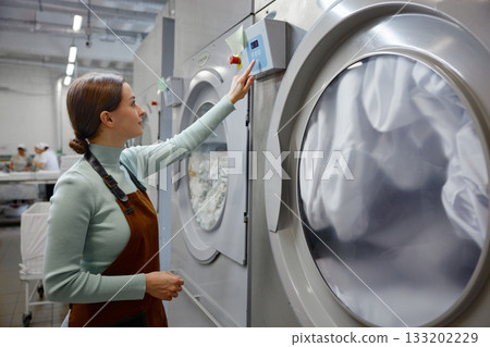 A woman is pressing down on a button on a washing machine 133202229