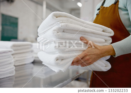Closeup of a woman worker in an apron holds fresh towels in a laundromat Closeup of a woman worker in an apron holds fresh towels in a laundromat 133202233