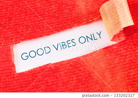 Red textured paper is torn open to reveal the message GOOD VIBES ONLY in a teal typeface. A sliver of white paper can be seen, curling at the top right corner 133202327