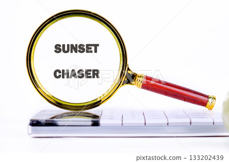 A vintage magnifying glass highlights the words Sunset Chaser on a tablet laying on top of a computer keyboard. The goal is to plan the next golden hour adventure A vintage magnifying glass highlights the words Sunset Chaser on a tablet laying on top of a computer keyboard. The goal is to plan the next golden hour adventure 133202439