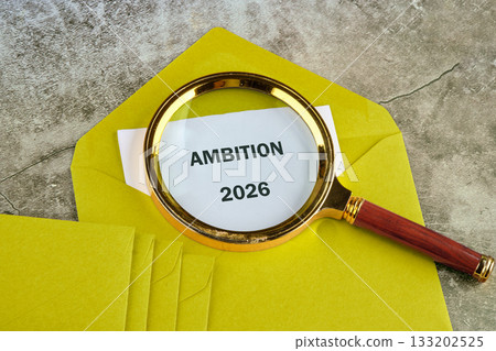 A yellow envelope holds a message about ambition for 2026, with a magnifying glass emphasizing the importance of future aspirations and planning for success 133202525