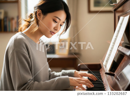 A woman with her hair tied up plays an upright piano with a serious expression 133202687
