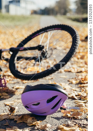 Purple helmet lies abandoned on the pavement beside a toppled bicycle, evidence of a sudden fall. Purple helmet lies abandoned on the pavement beside a toppled bicycle, evidence of a sudden fall. 133202893