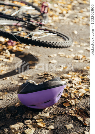 Purple helmet lies abandoned on the pavement beside a toppled bicycle, evidence of a sudden fall. Purple helmet lies abandoned on the pavement beside a toppled bicycle, evidence of a sudden fall. 133202906