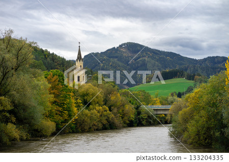 Panoramic view of the church spire among the autumn city against the background of the Austrian Alps and the river 133204335