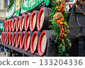 Many wooden wine barrels stacked on top of each other on a cart decorated with flowers for the harvest festival. 133204336