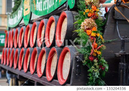 Many wooden wine barrels stacked on top of each other on a cart decorated with flowers for the harvest festival. 133204336