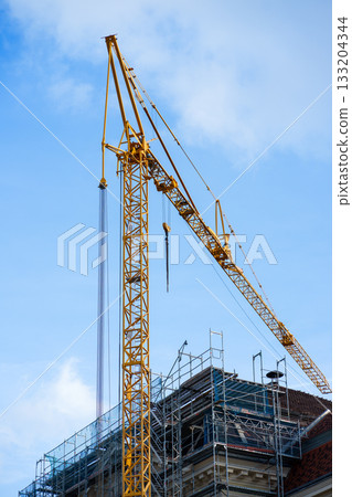 Construction site with a tall yellow crane and metal scaffolding on a historic building under renovation. Equipment for construction workers Construction site with a tall yellow crane and metal scaffolding on a historic building under renovation. Equipment for construction workers 133204344
