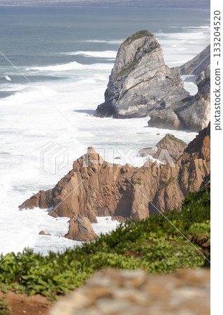 Dramatic rocky cliffs of Cabo da Roca rising above the Atlantic Ocean, with powerful waves crashing below and stunning coastal scenery. 133204520