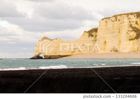 Limestone sea cliffs and natural arch at Etretat, Normandy, framed by ocean waves and a calm coastal landscape. Limestone sea cliffs and natural arch at Etretat, Normandy, framed by ocean waves and a calm coastal landscape. 133204606