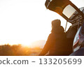 A man opens the trunk of his car and watches the sunrise 133205699