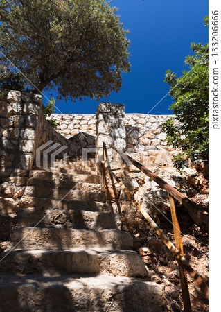 A rugged stone staircase climbs beside a weathered stone wall under a clear blue sky 133206666