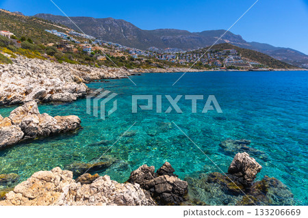 Wild beach Kalkan landscape photo. Turquoise waters lap a rugged rocky coast Wild beach Kalkan landscape photo. Turquoise waters lap a rugged rocky coast 133206669