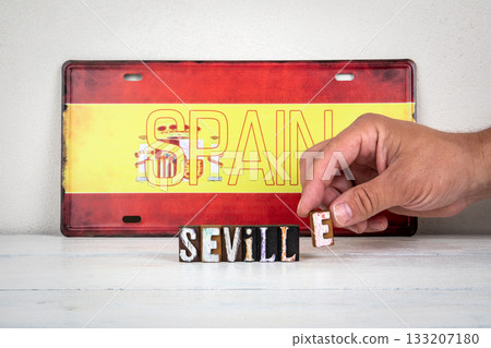Hand placing wooden letter E to form the word Seville in front of Spain flag license plate, travel Hand placing wooden letter E to form the word Seville in front of Spain flag license plate, travel 133207180