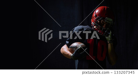 Football player holding ball with emotional fatigue in dramatic low light Football player holding ball with emotional fatigue in dramatic low light 133207345