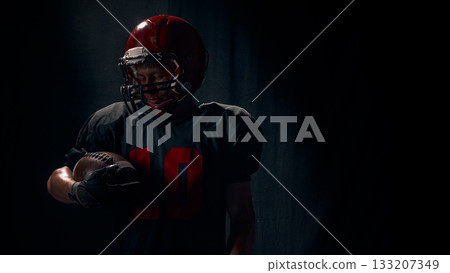 Football player holding ball with quiet reflective emotion under spotlight Football player holding ball with quiet reflective emotion under spotlight 133207349