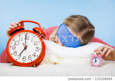 Sleeping woman wearing pajamas holding clock Sleeping woman wearing pajamas holding clock 133208984