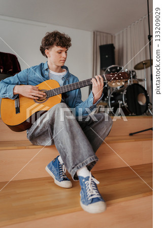 Teenage boy playing acoustic guitar in school music room. 133209029